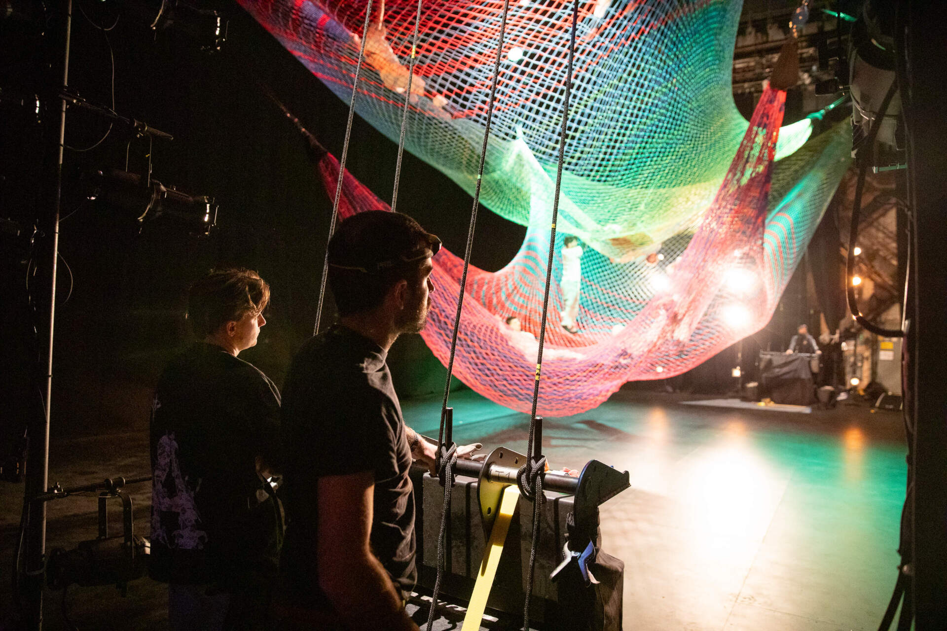 Two riggers stand towards the left of the stage, ready to adjust the height of sculptor Janet Echelman’s two 40-foot by 30-foot nets. (Artemisia Luk/WBUR)