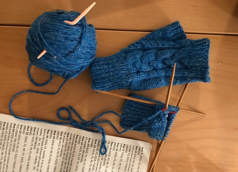 A ball of yarn, gloves in progress and a knitting book. (Courtesy Ariel Katz)
