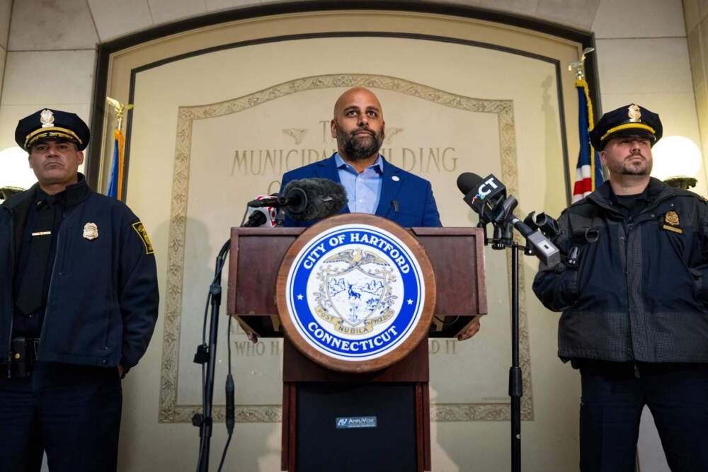 Hartford Mayor Arunan Arulampalam (center) responds to incidents at a protest against ICE the night before during which suspected federal employees used pepper spray on protesters, one protester was struck by a suspected federal vehicle, and a window on the vehicle was broken by a protester. (Tyler Russell/Connecticut Public)