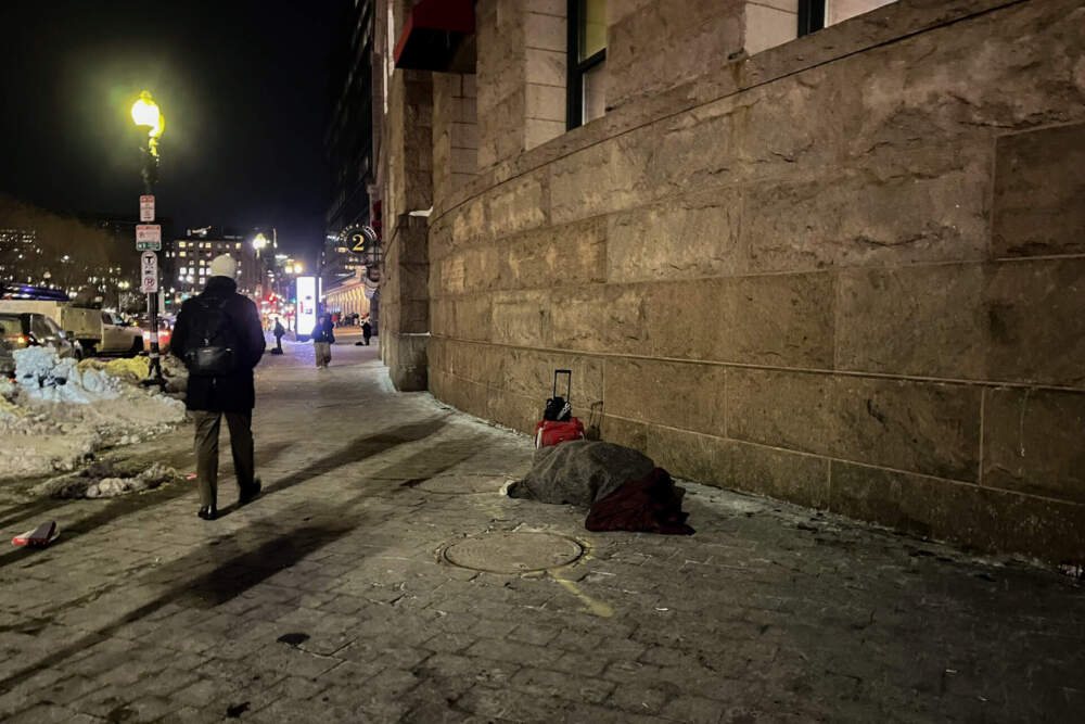 Someone lies covered in blankets outside South Station in Boston. (Lynn Jolicoeur/WBUR)