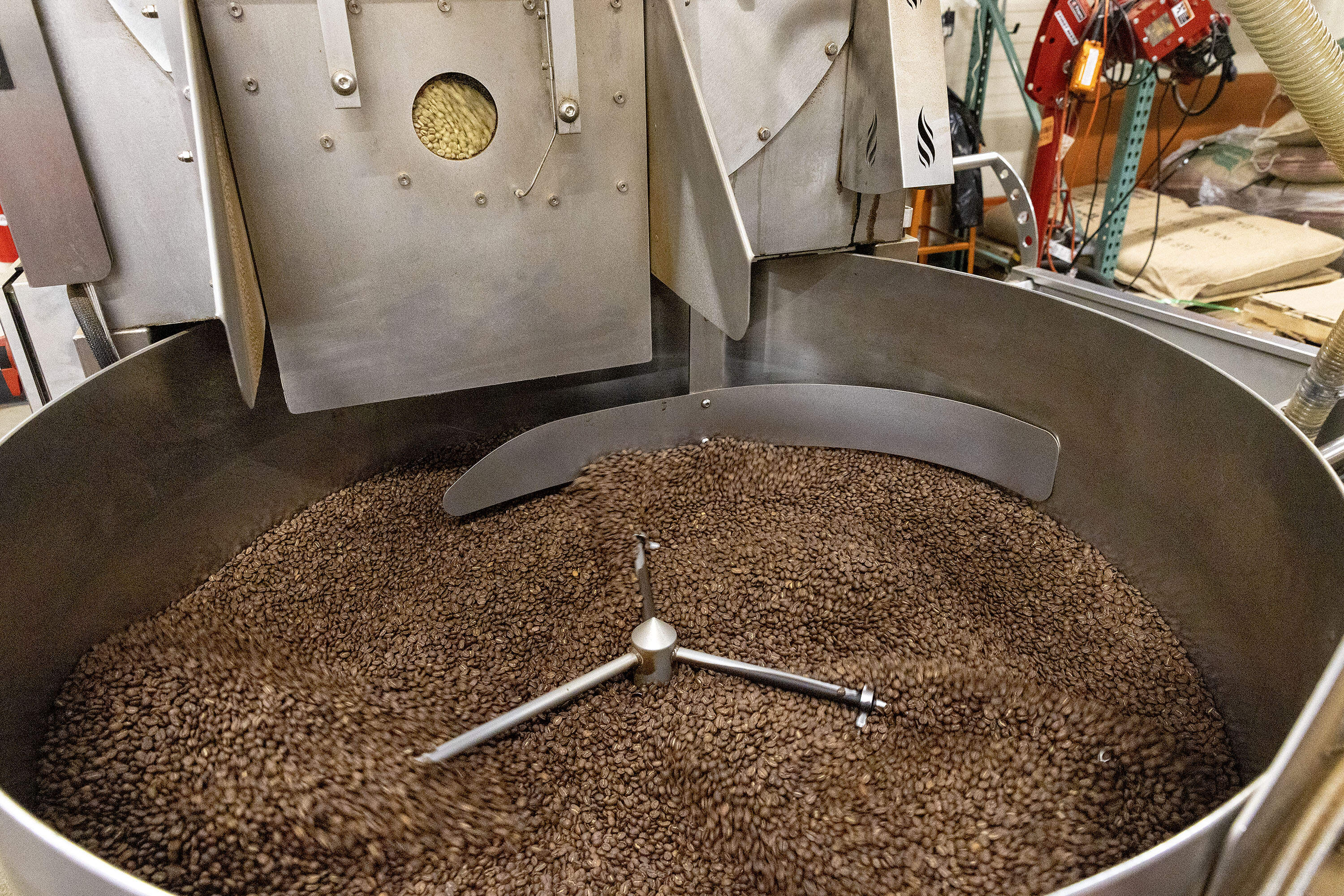 A coffee roasting machine at the George Howell roastery in Acton, Mass. cools roasted coffee beans in a cooling tray outside the oven. Inside the oven, the next batch of green coffee beans is visible through a small round window, at the start of the roasting process. (Robin Lubbock/WBUR)