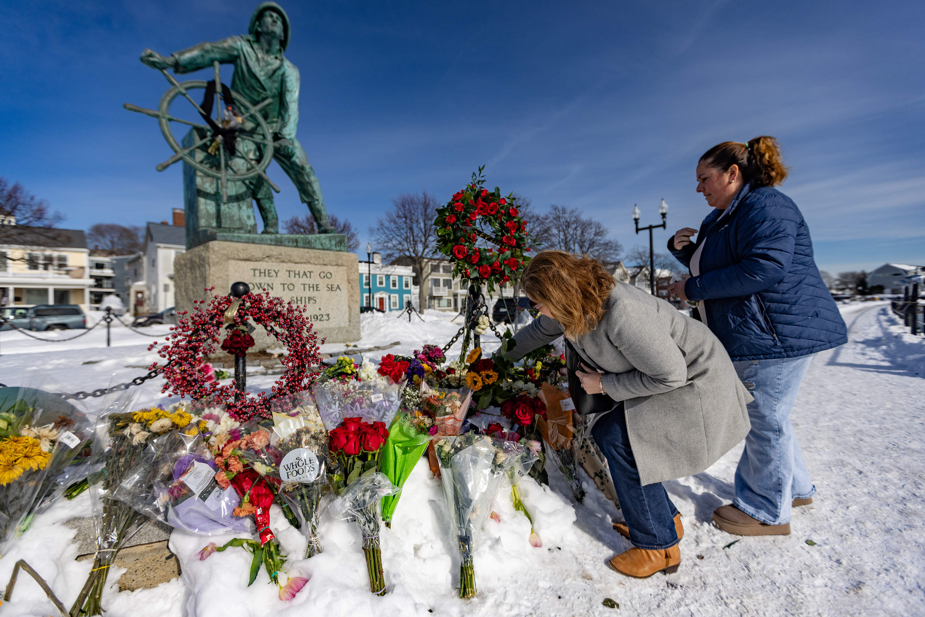 Susan Picariello and Susan Russo leave flowers to remember those lost on the Lily Jean at the Fisherman’s Memorial in Gloucester. (Jesse Costa/WBUR)