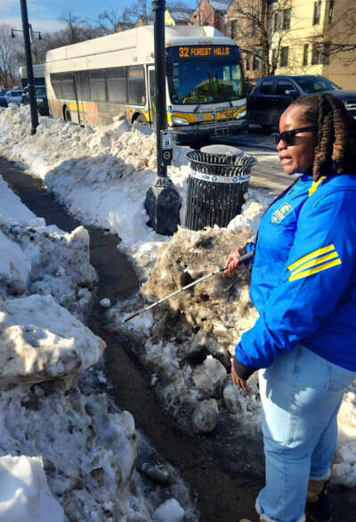 Boston resident Casandra Xavier demonstrates how the narrowly shoveled sidewalk prohibits her from properly using her white cane to walk on Hyde Park Avenue in Jamaica Plain on Feb. 4. (Andrea Perdomo Hernandez/WBUR)