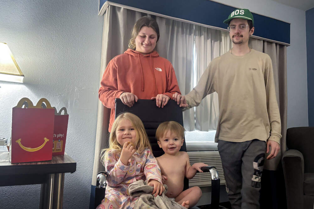Mackenzie Rattigan and Zachary Rebelo stand next to their children by the heater in a Sandwich hotel room. (Eve Zuckoff/WBUR)