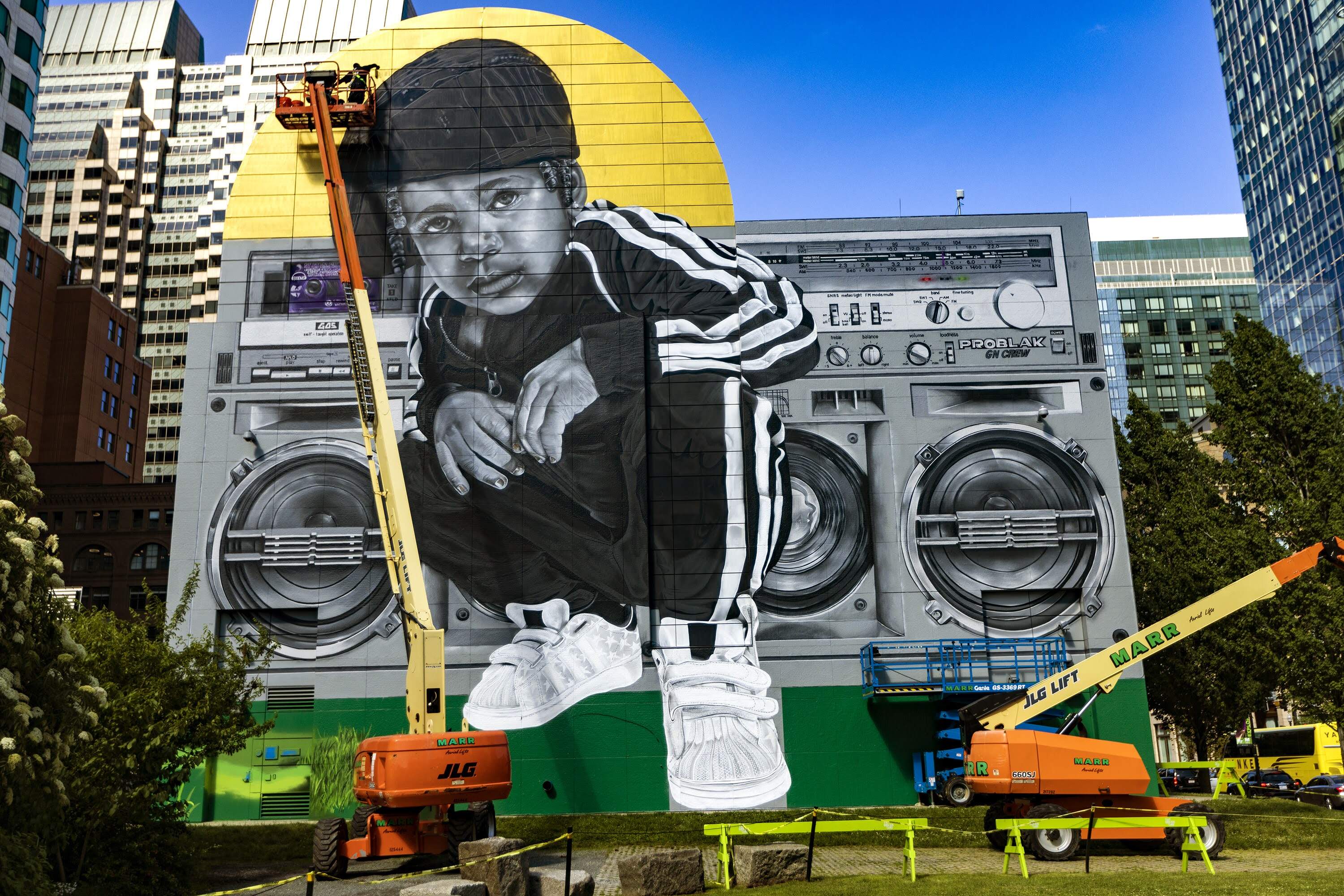 High above on a knuckle lift, Rob “ProblaK” Gibbs works on “Breathe Life Together,”  featured on the façade of the Dewey Square Tunnel Air Intake Structure on the Rose Kennedy Greenway in 2022. (Jesse Costa/WBUR)