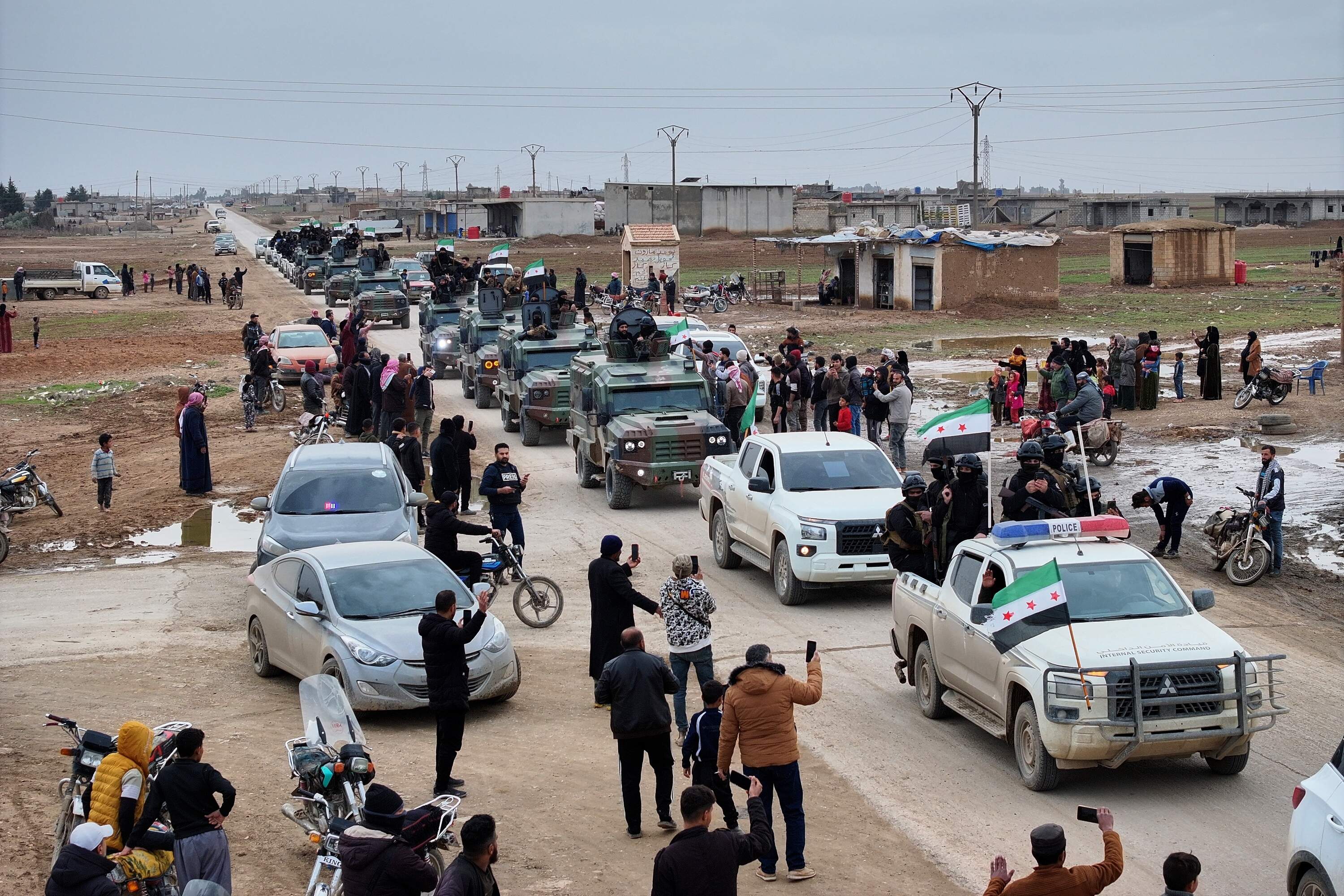 Local residents, predominantly Arab, welcome a convoy of Syria's Interior Ministry forces as it passes through en route to the mostly Kurdish town of Qamishli, where the forces are deploying under a ceasefire agreement with the Kurdish-led Syrian Democratic Forces (SDF), in the village of Mazraat al-Nahar, northeastern Syria, Tuesday, Feb. 3, 2026. (Ghaith Alsayed/AP)