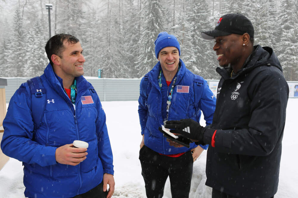 United States' bobsledders Frank Del Duca, left and Boone Niederhofer speak with De Aundre John, right, a bobsledder from Trinidad and Tobago after trading their unique national team pins, at the Cortina Olympic Village. (Jennifer McDermott/AP)