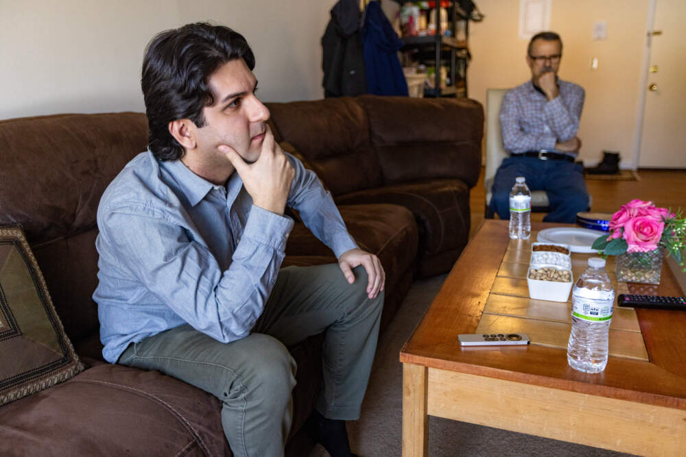 Hawreh Haddadi, left, and his father Karim watch Iran International News on television to find out the latest news about the war in Iran. (Jesse Costa/WBUR)