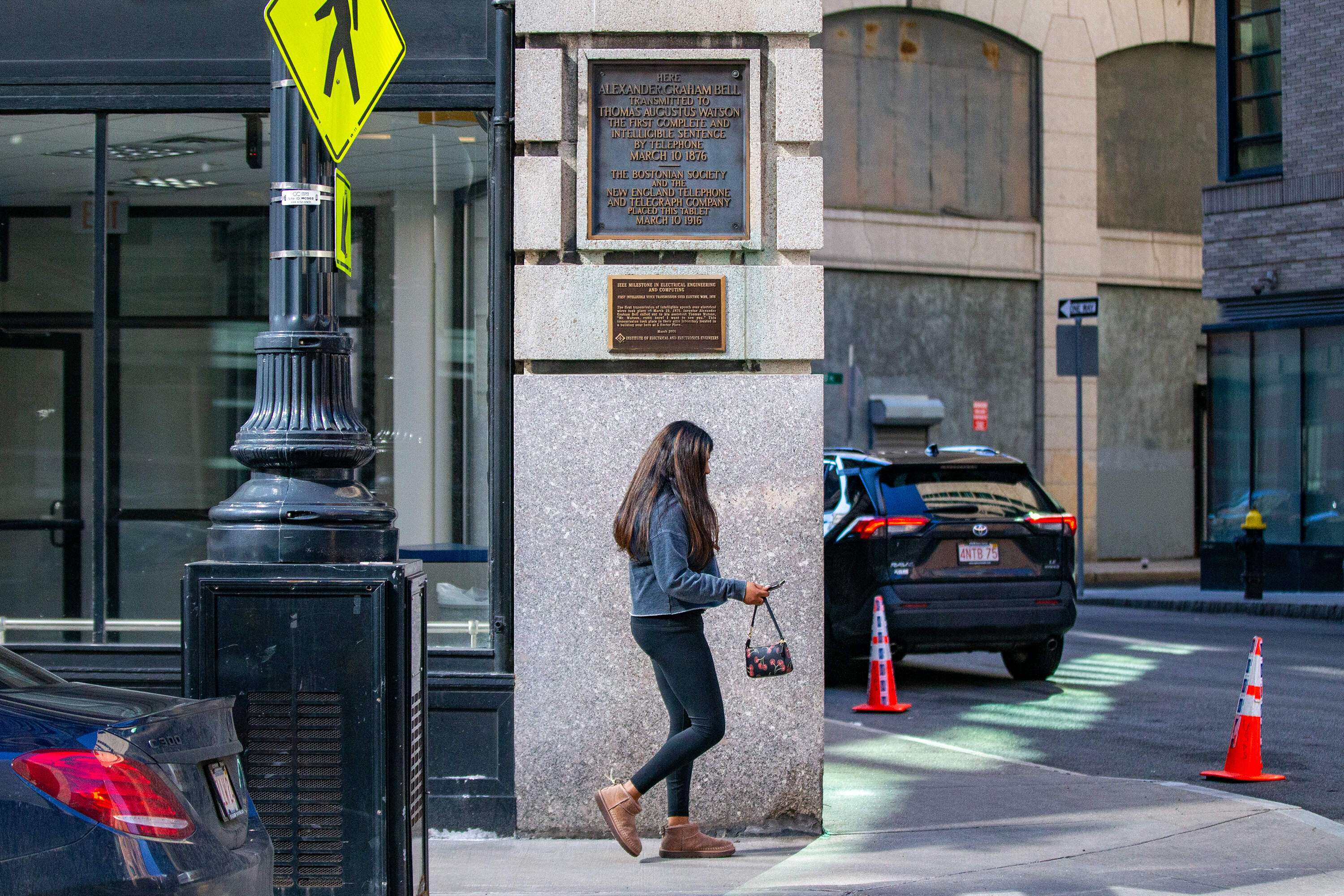 A young woman looks at her smart phone as she walks past the plaque on Avenue de Lafayette marking the place where, Alexander Graham Bell transmitted to Thomas Watson, the first complete and intelligible sentence by telephone. (Jesse Costa/WBUR)