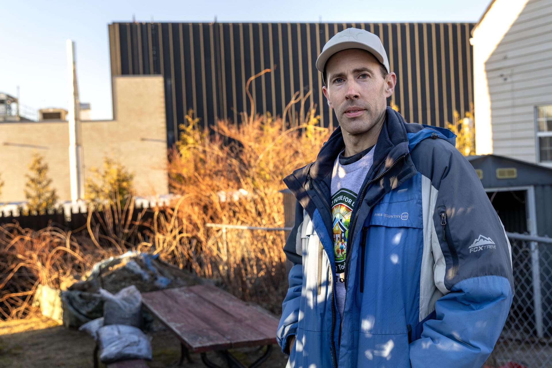 Jake Fortes stands in his yard with Markley's Lowell data center behind him. (Robin Lubbock/WBUR)