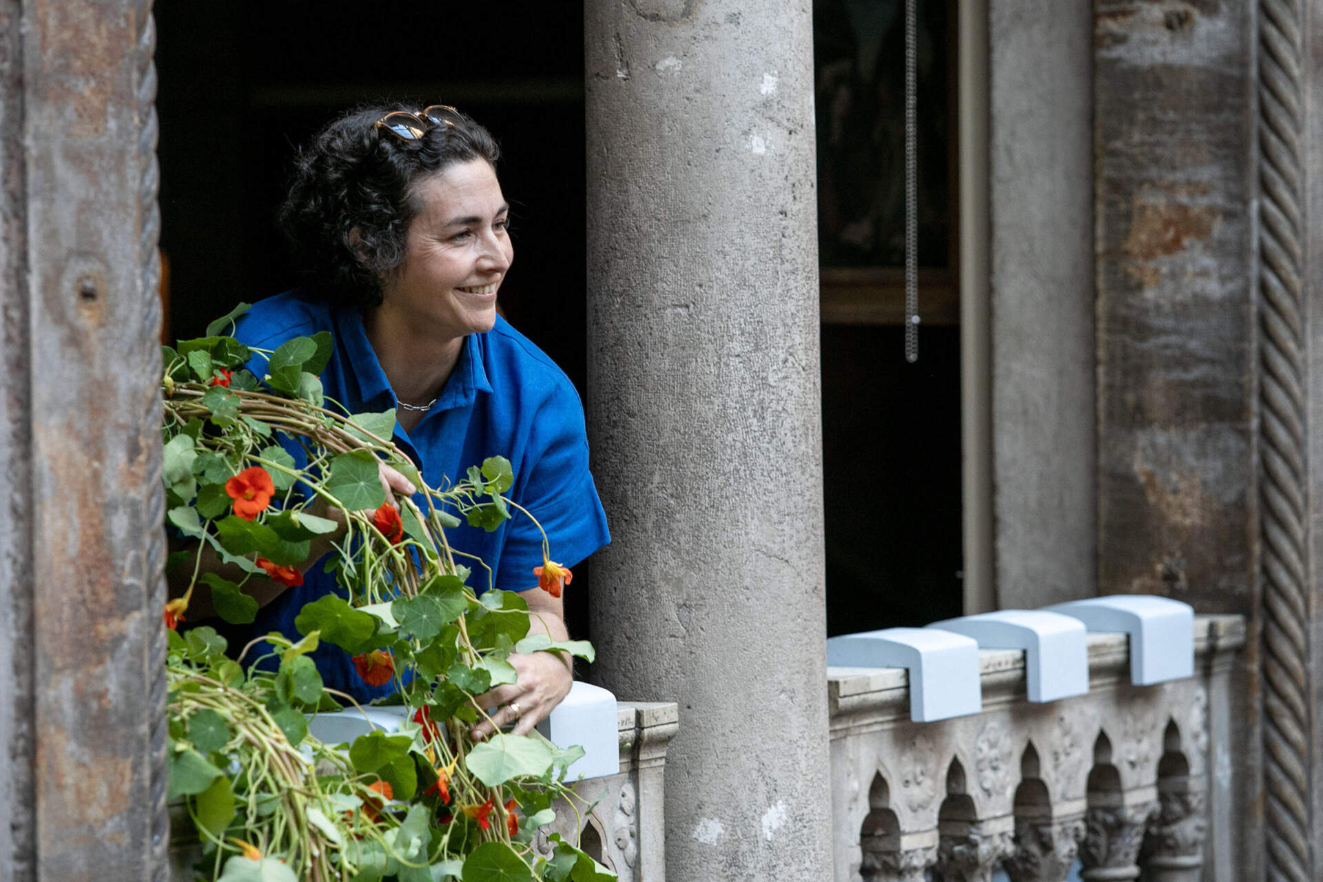With the help of a colleague across the courtyard, Director of Horticulture Erika Rumbley positions a nasturtium vine in a window of the Titian Room at the Isabella Stewart Gardner Museum. (Robin Lubbock/WBUR)