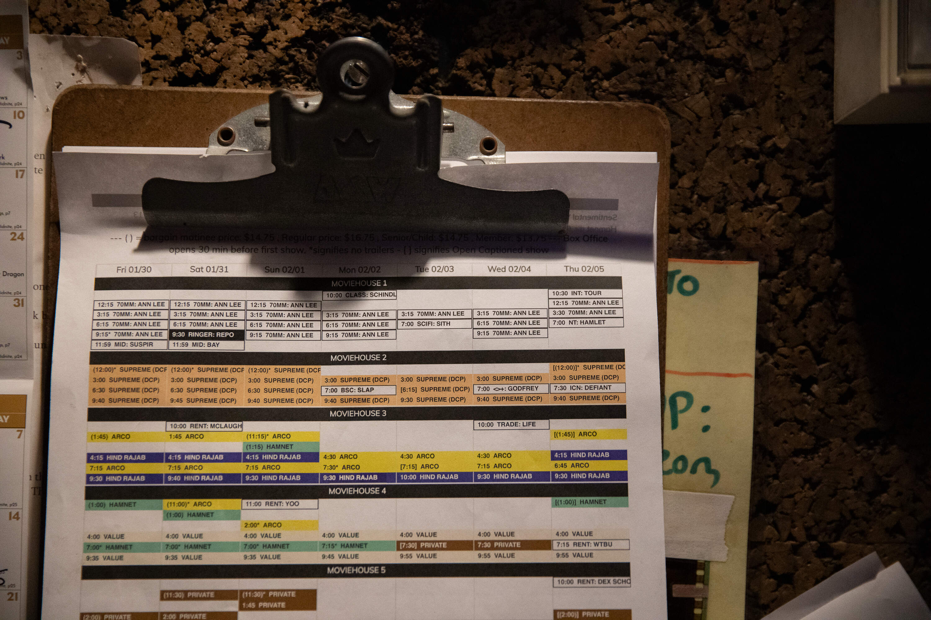 Printouts on a clipboard list Coolidge Corner Theater’s film lineup for a week in early February. Twenty 70 mm showings of "The Testament of Ann Lee" were scheduled. (Artemisia Luk/WBUR)