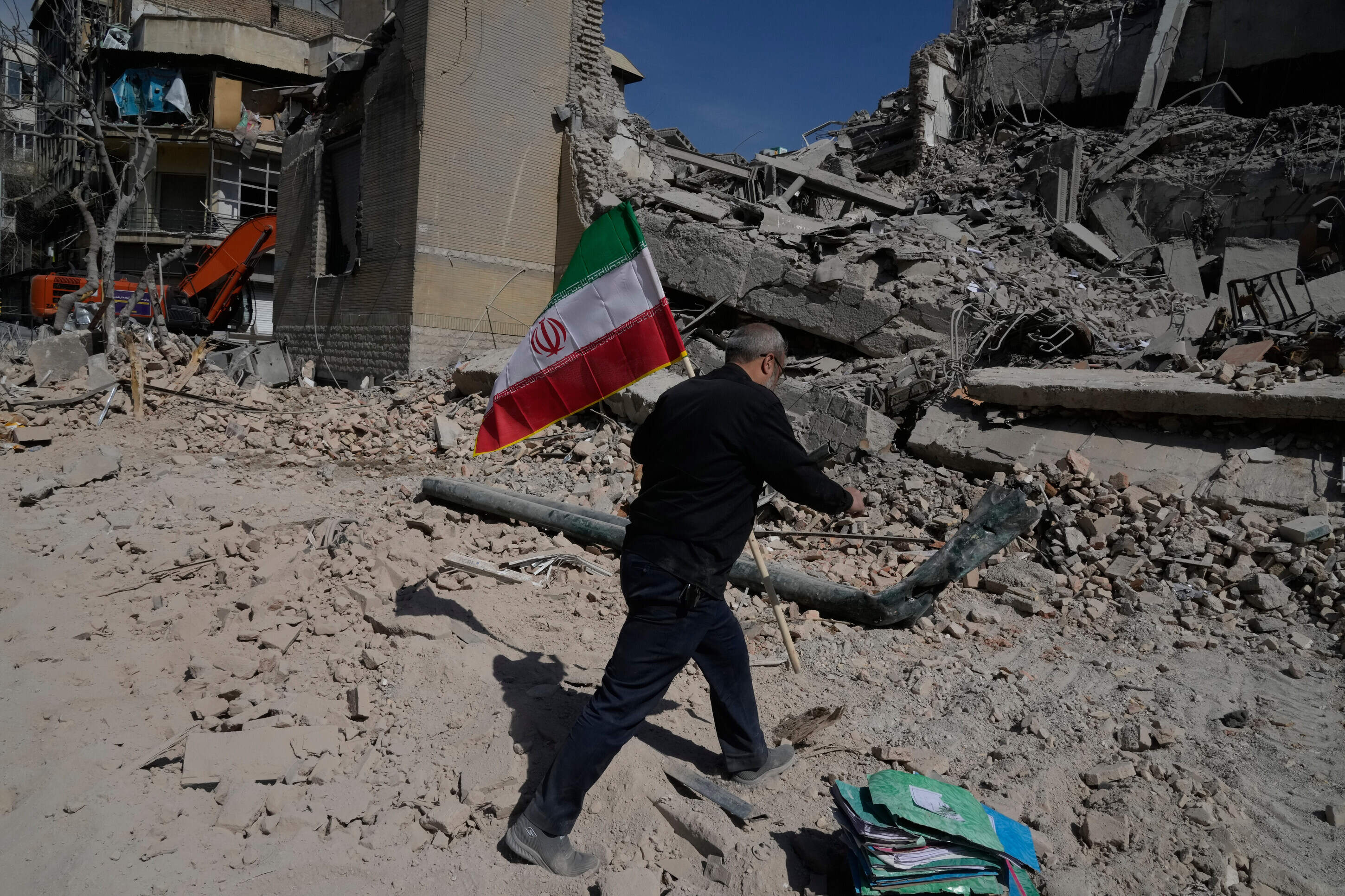 A man carries an Iranian flag to place on the rubble of a police facility struck during the U.S.–Israeli military campaign in Tehran, Iran, Wednesday, March 4, 2026. (Vahid Salemi/AP)