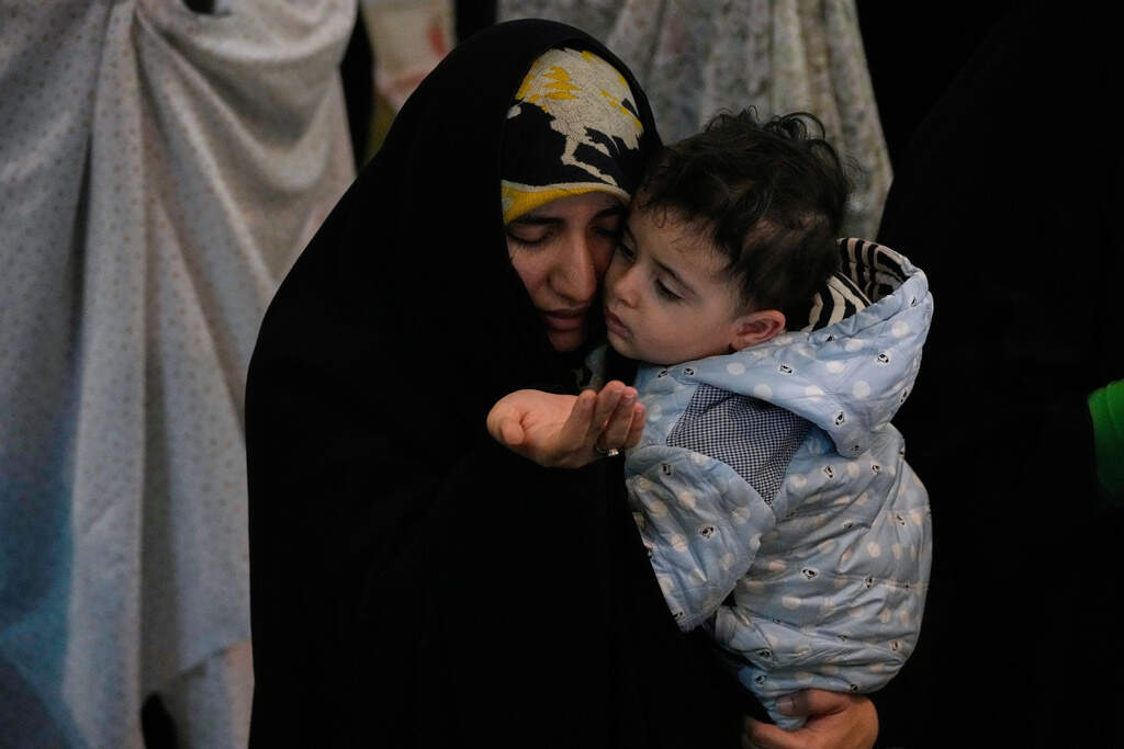 An Iranian worshipper prays during a ceremony to perform Eid al-Fitr prayers marking the end of the holy fasting month of Ramadan while holding a child at the Imam Khomeini Grand Mosque in Tehran, Iran, Saturday, March 21, 2026. (AP Photo/Vahid Salemi)