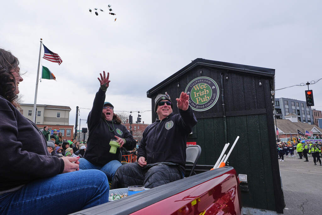 Dena Taylor and Tony DiDonato, right, toss candy to spectators while riding in a truck hauling the "Wee Irish Pub" during the annual St. Patrick's Day parade through Southie, Sunday, March 15, 2026. (Charles Krupa/AP)