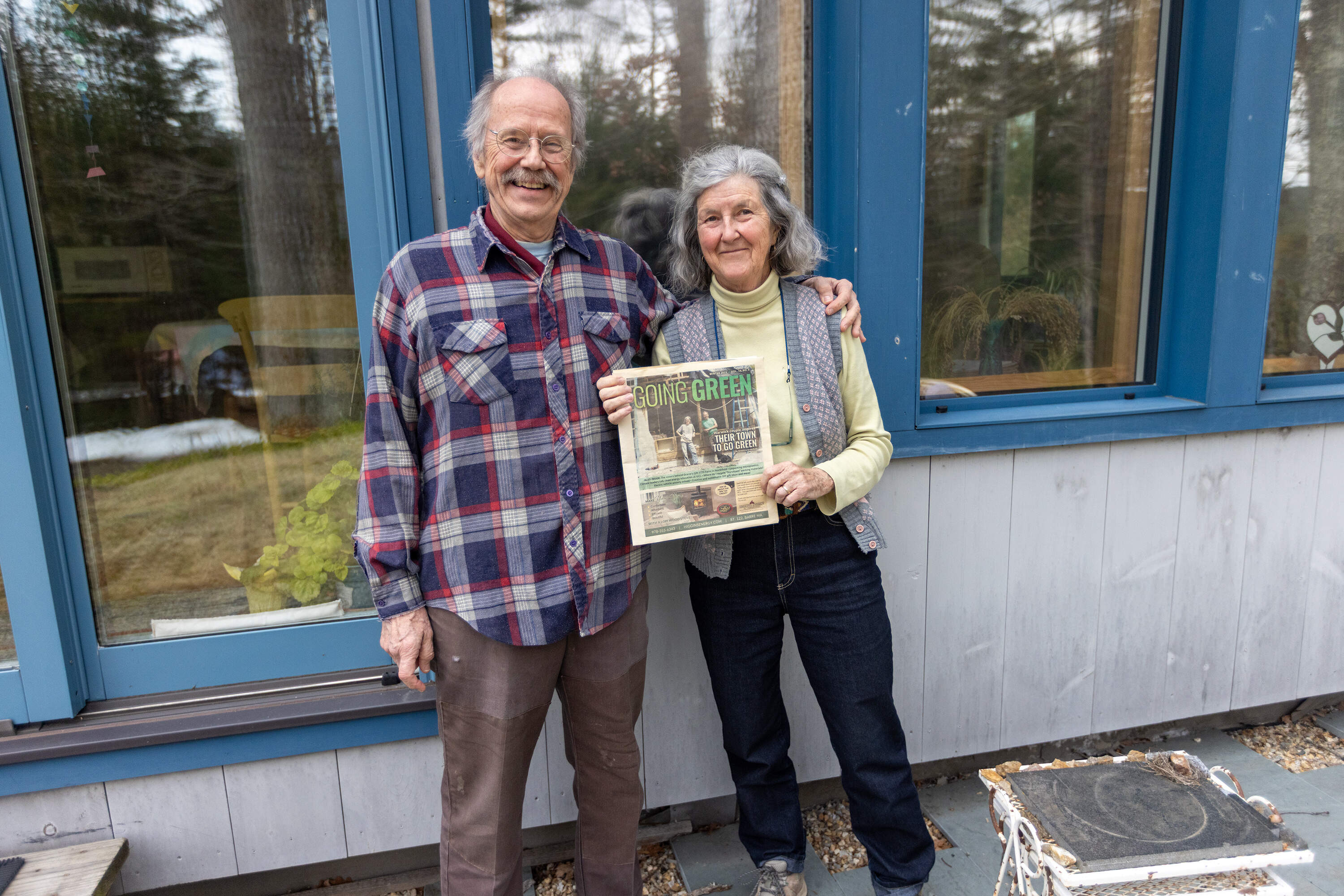 Stephen and Janice Kurkoski standing out in front of their home in Warwick holding a copy of the Going Green publication, which features the couple and their quest to make their town run solely on electric power. (Jesse Costa/WBUR)