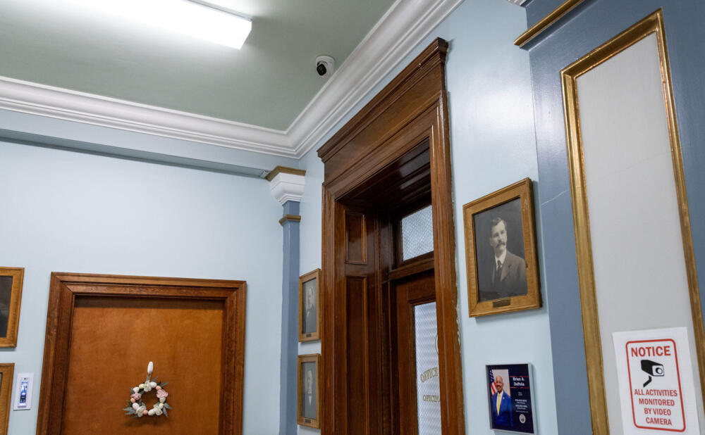 A camera attached to the ceiling, and a sign warning visitors about live video cameras, inside Lawrence City Hall by the mayor's office. (Robin Lubbock/WBUR)