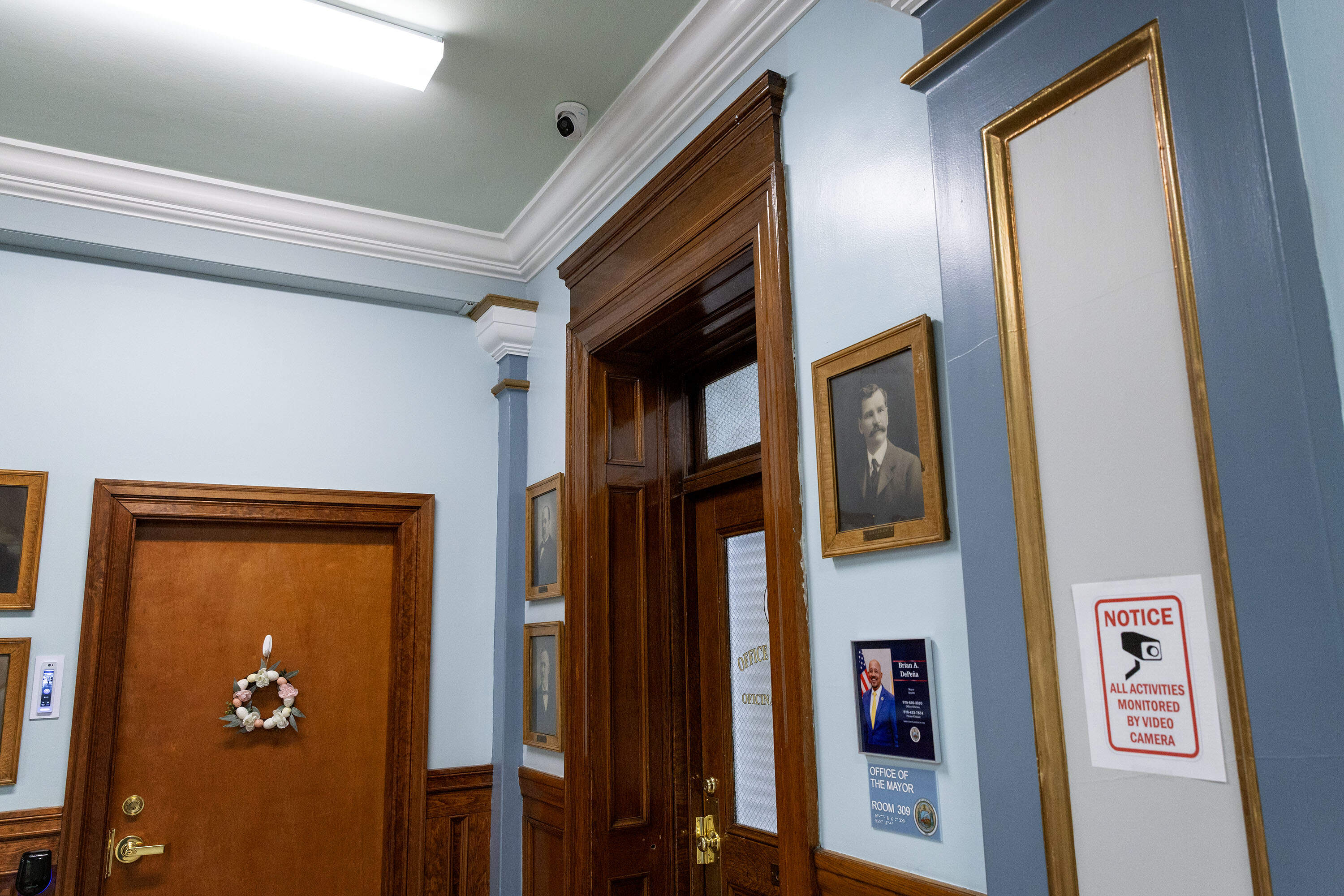 A camera attached to the ceiling, and a sign warning visitors about live video cameras, seen near the mayor's third floor office at Lawrence City Hall. (Robin Lubbock/WBUR)