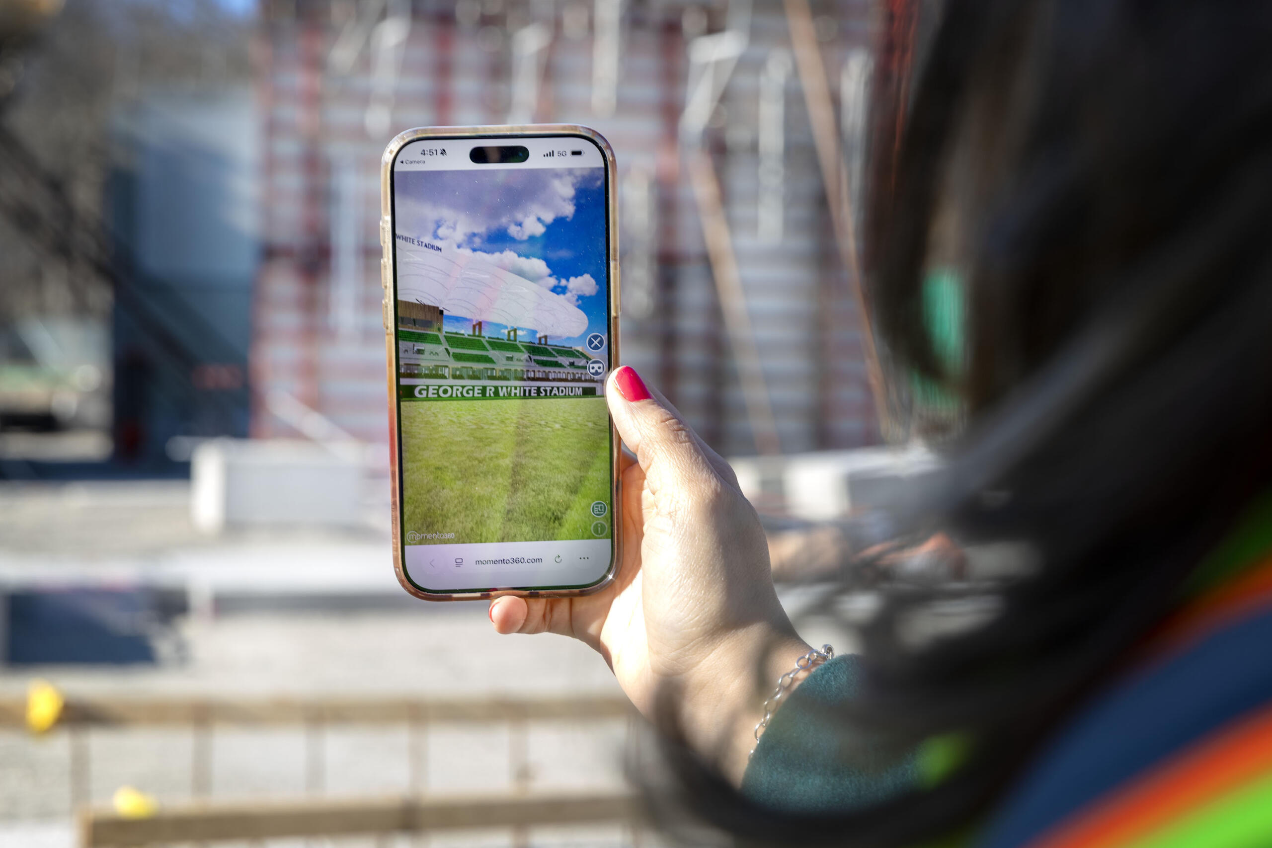 Diana Fernandez Bibeau, deputy chief of urban design at the Boston Planning Department, looks at a virtual reality image of the finished White Stadium, as she stands in the midst of construction for the stadium's east grandstand. (Robin Lubbock/WBUR)
