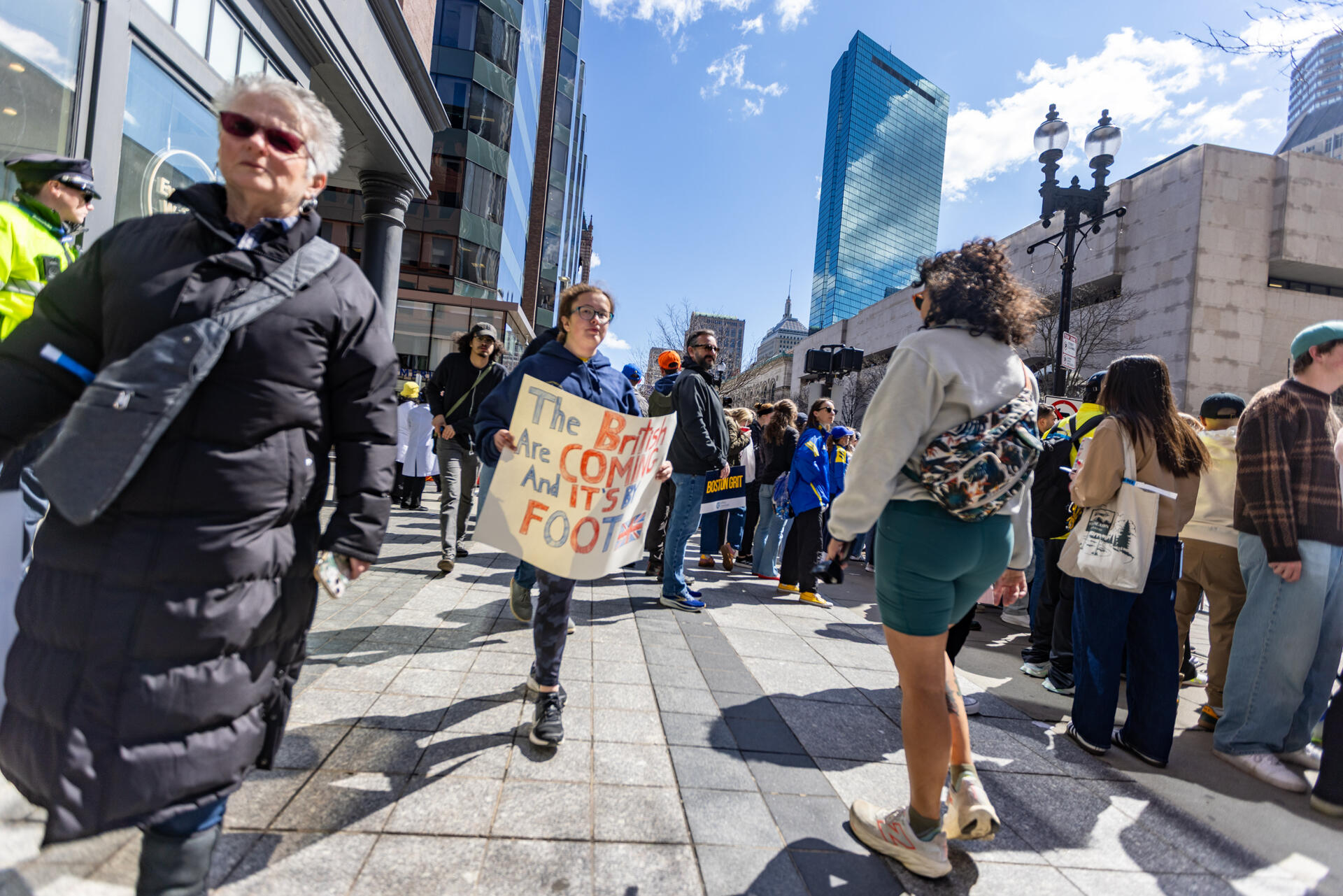 A woman walks down Boylston Street holding a sign that reads, “The British are coming and it’s on foot," during the Boston Marathon. (Jesse Costa/WBUR)