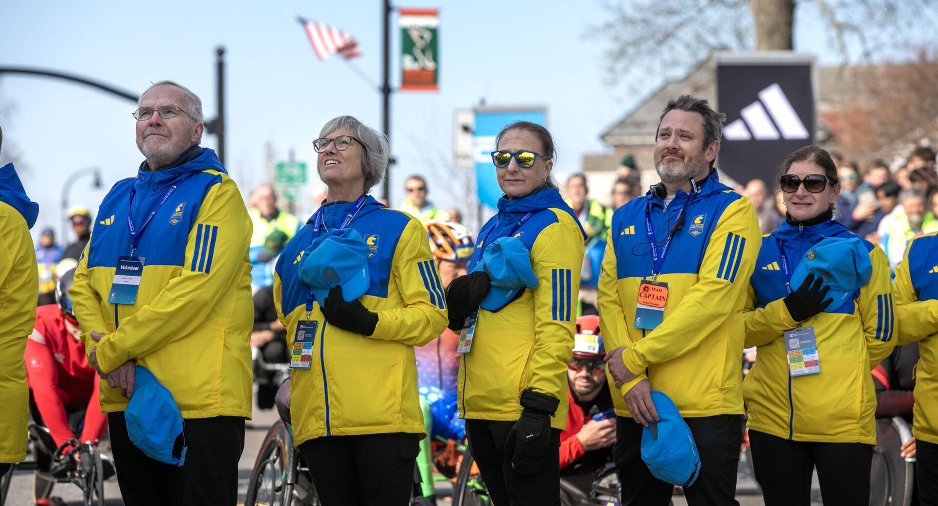 Course volunteers listen to the National Anthem at the start line of the 130th Boston Marathon. (Robin Lubbock/WBUR)