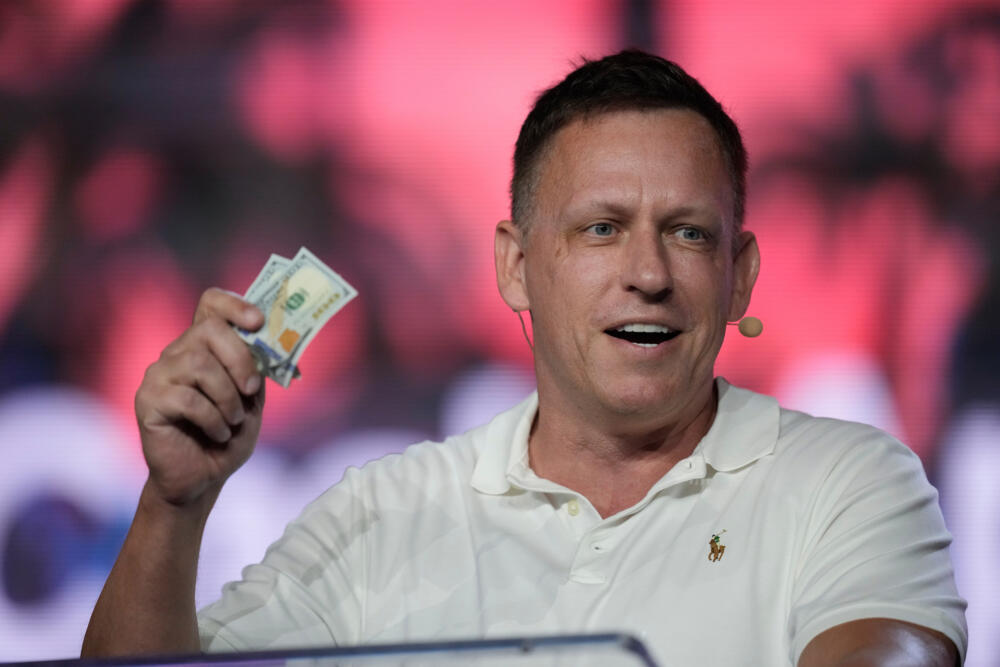 FILE - Peter Thiel, co-founder of PayPal and Palantir, offers a pair of hundred dollar bills to attendees during a keynote address at the Bitcoin Conference, April 7, 2022, in Miami Beach, Fla. (Rebecca Blackwell/AP)