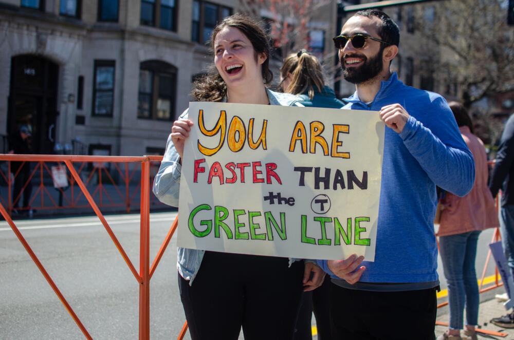 Sheila Baker and Dean Pacilli of Cambridge with a sign inspired by the MBTA in 2022. (Sharon Brody/WBUR)
