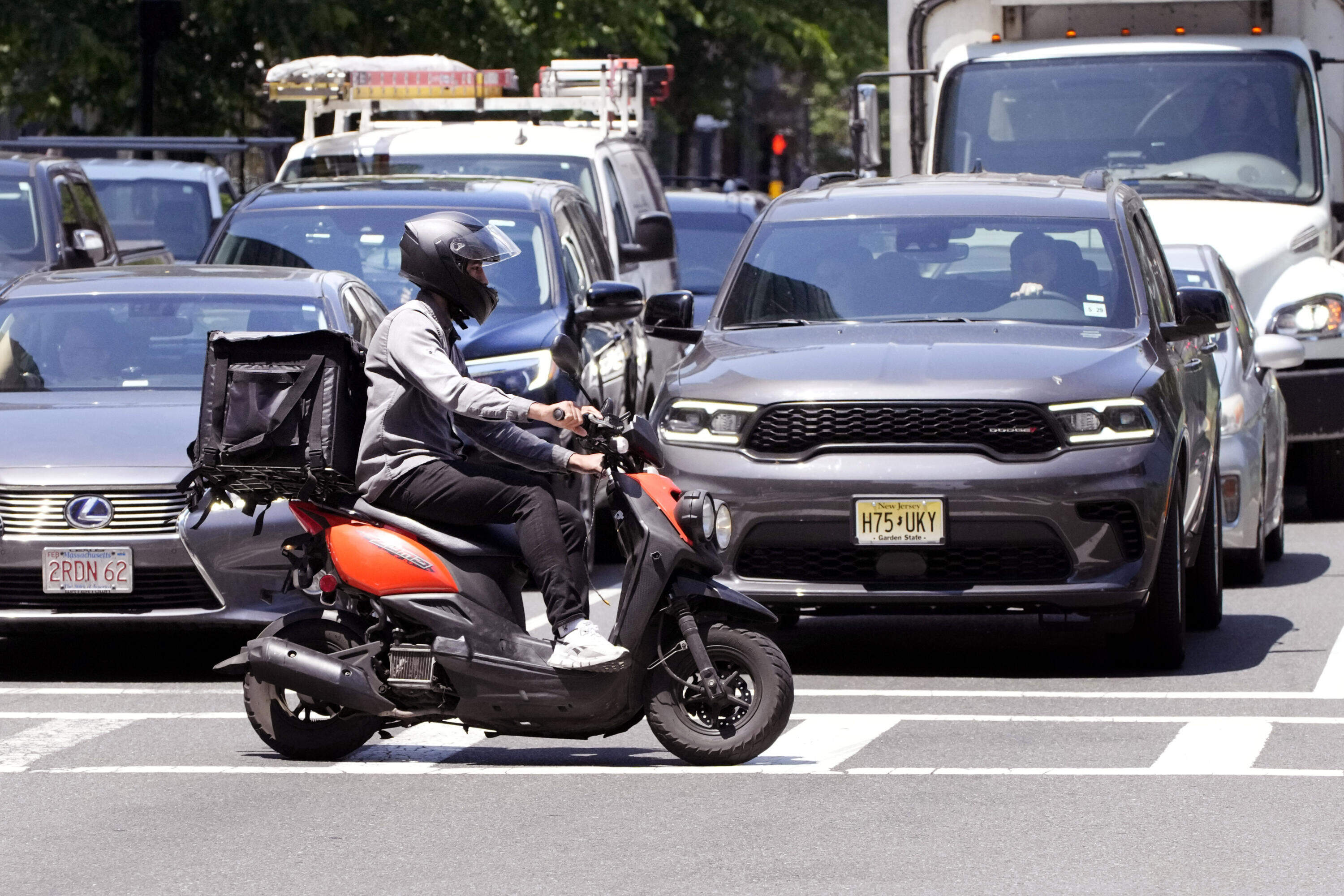 A delivery driver on a scooter rides the pedestrian crosswalk through traffic on a delivery in the Seaport District, Friday, June 7, 2024, in Boston. (Charles Krupa/AP)