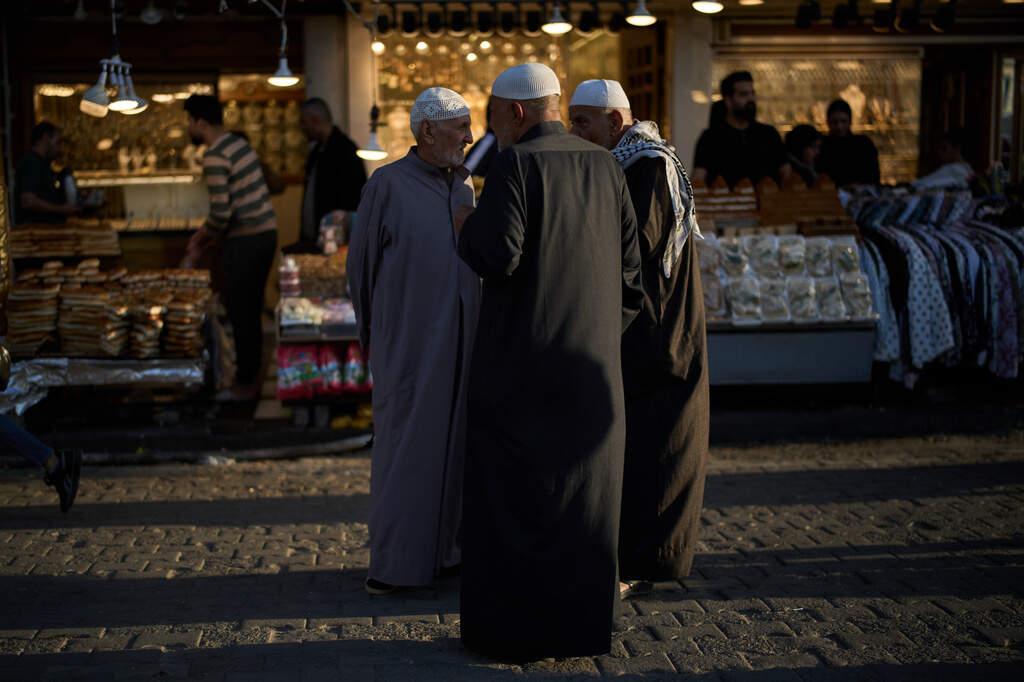 Elderly Muslim men talk at a market near the Kadhimiya Shrine at dusk in the Shiite neighbourhood of Baghdad, Iraq, Tuesday, March 31, 2026. (AP Photo/Leo Correa)