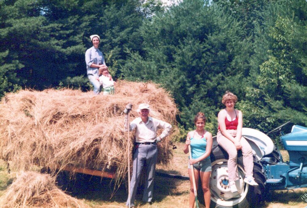 A young Jennifer Acker stands with her mom on top of a trailer of hay with her grandfather, cousin and half-sister below. (Courtesy Jennifer Acker)