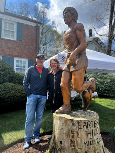 Mark Proctor and Charlotte McKee, of Newton, pose in front of the running statue on Heartbreak Hill. (Artemisia Luk/WBUR)