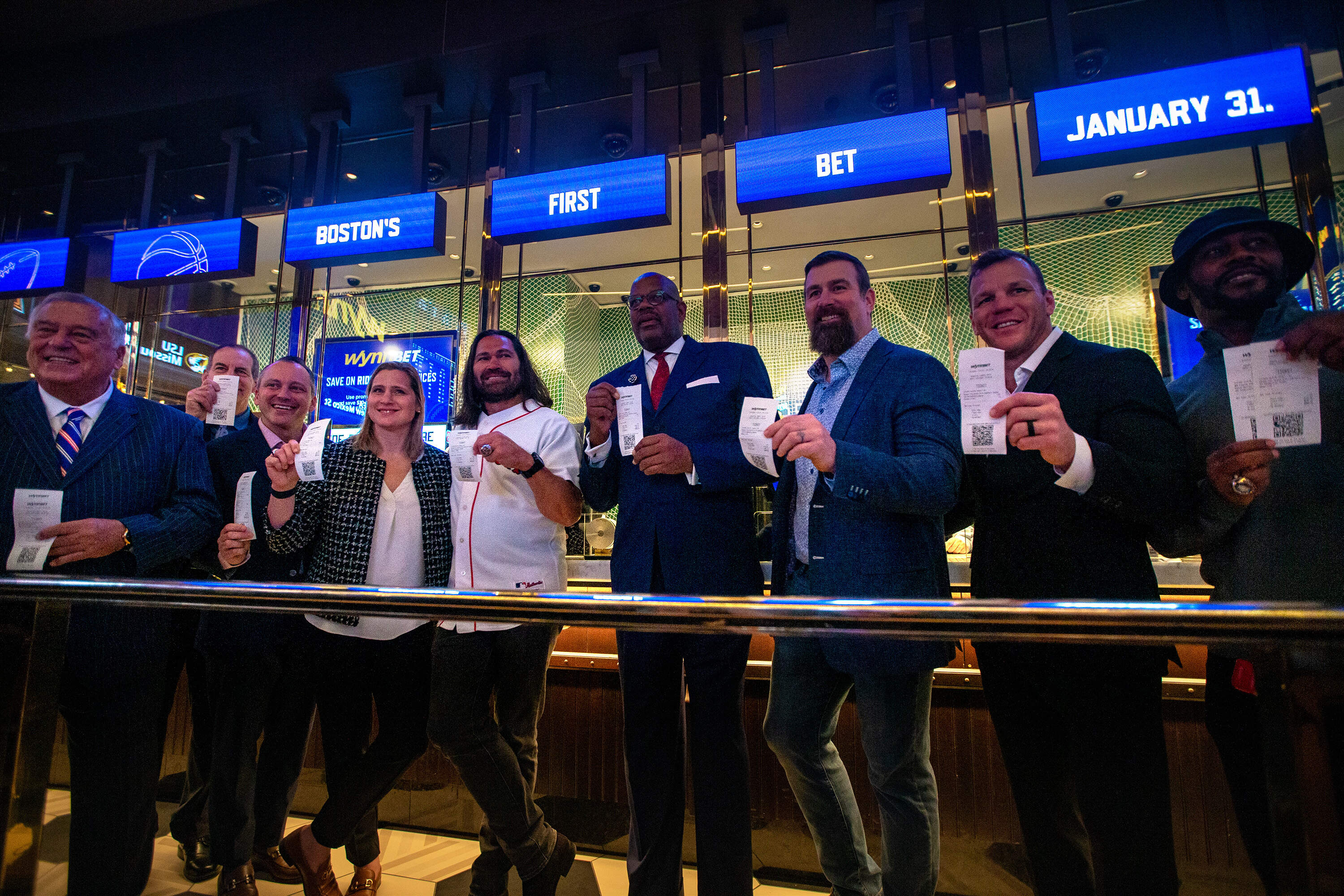 Boston championship-winning athletes and state representatives, including Speaker Ron Mariano (far left) show the first bets at the windows of the WynnBET Sportsbook at Encore Boston on Jan. 31, 2023. (Jesse Costa/WBUR)