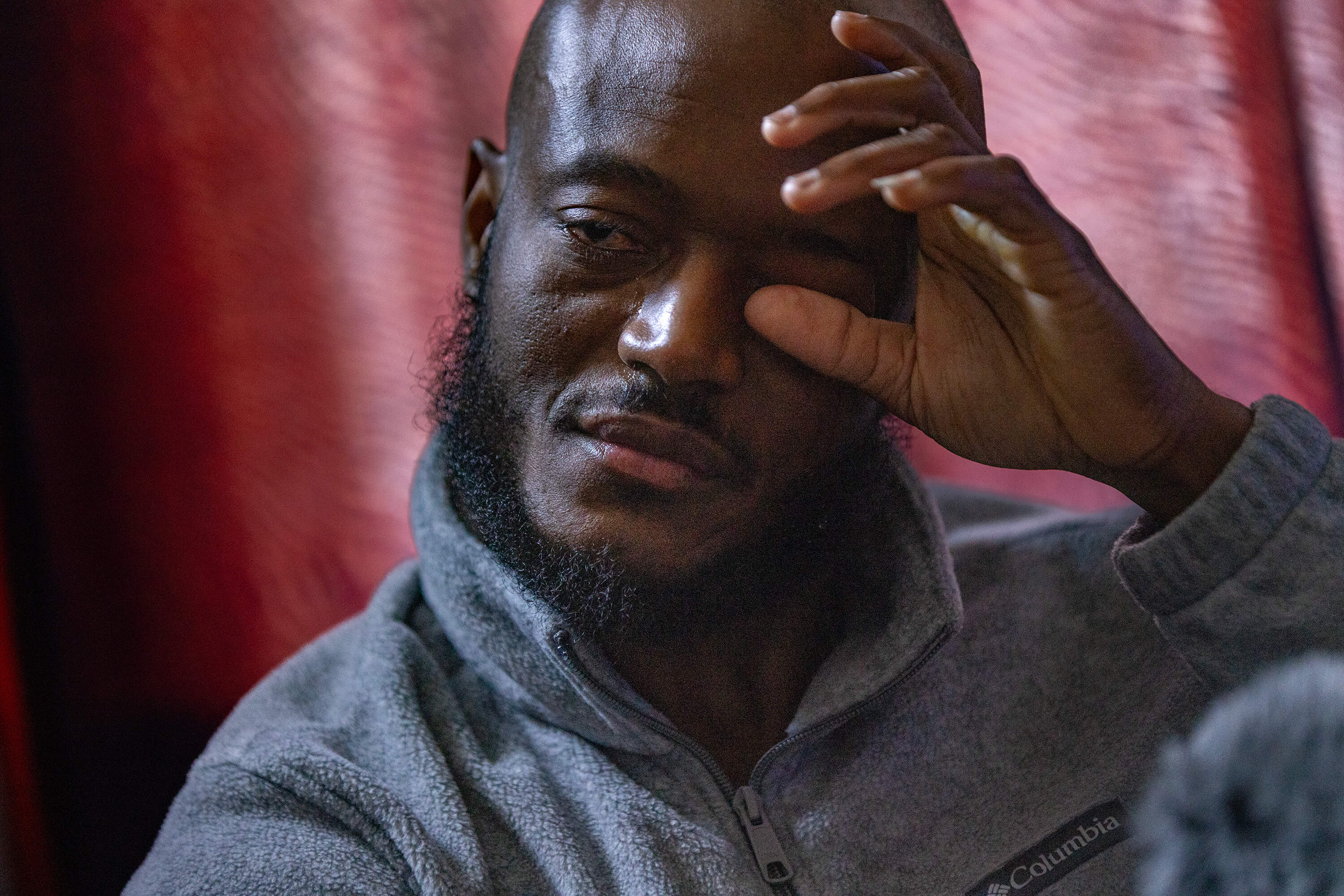A close up photograph of a man wiping a tear from his eyes.