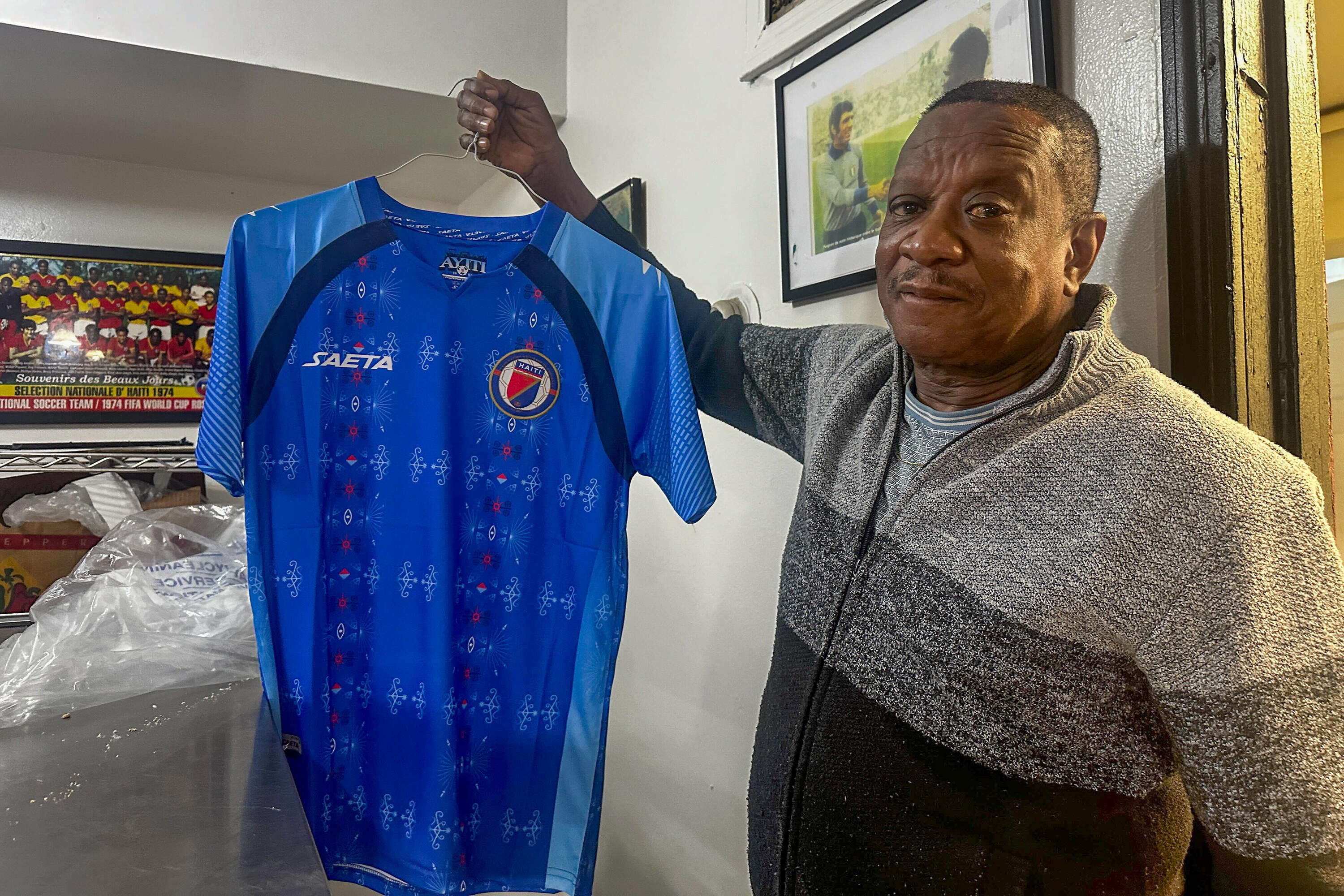 Frantz Guillaume, owner of Fan Fan Bakery in Hyde Park, shows off one of the Haiti jerseys for sale at the bakery. So far, he's sold 150 of them. (Simón Rios/WBUR)