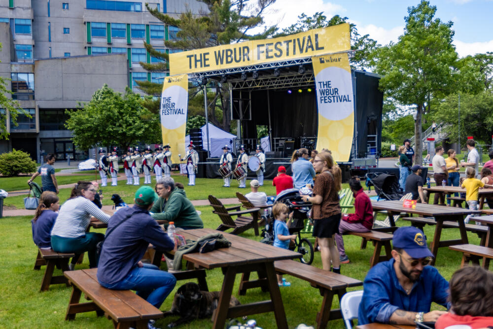 Festival goers sit at picnic tables while the Middlesex County Volunteers of Massachusetts play fife and drum at The WBUR Festival in 2025. (Jesse Costa/WBUR)