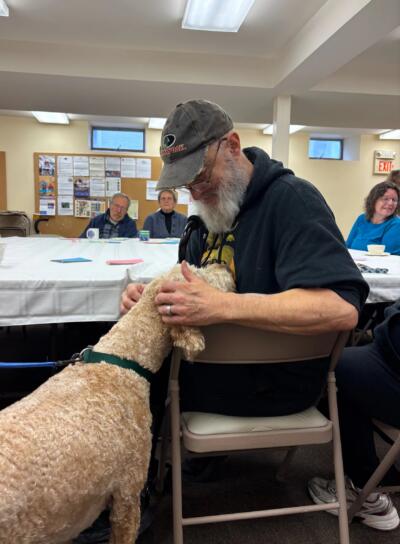 John Yaffee of North Springfield scratches Dusty, a therapy dog that occasionally comes to the memory cafe in Chester. (Nina Keck/Vermont Public)