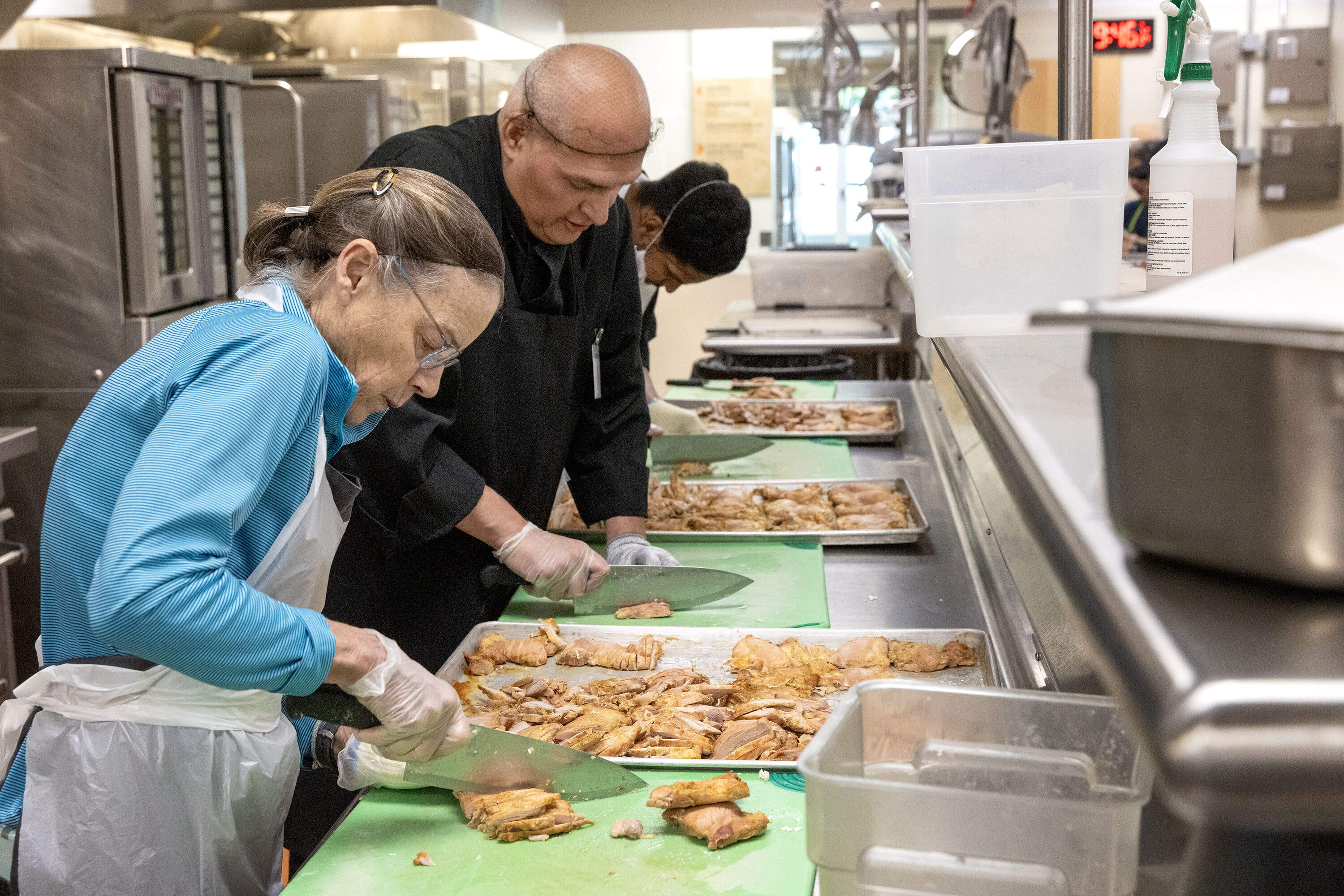 Volunteers and staff slice curried chicken in the kitchen at Community Servings in Jamaica Plain, Mass. (Robin Lubbock/WBUR)