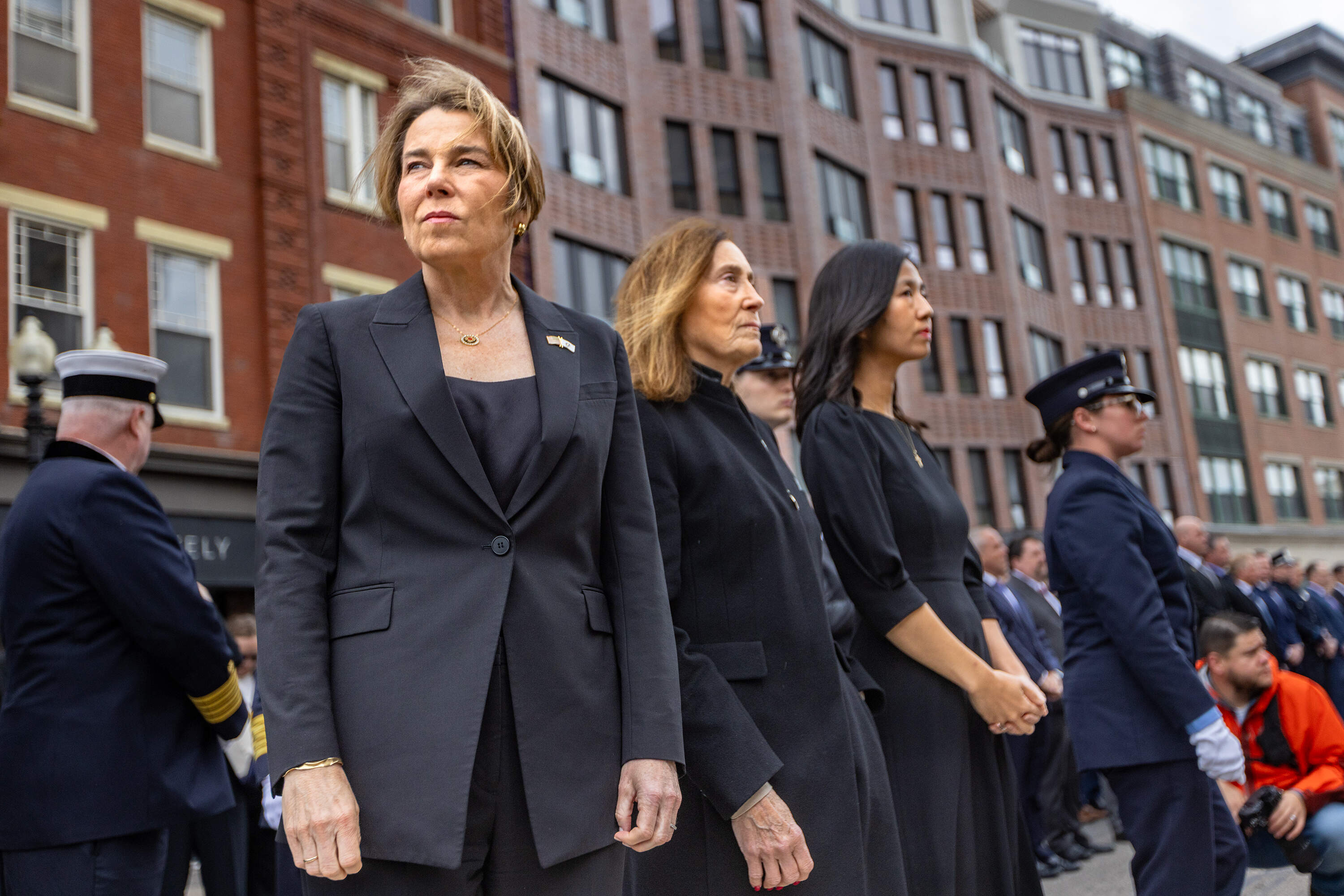 Gov. Maura Healey, State Treasurer Deb Goldberg and Mayor Michelle Wu watch as firefighters stream into the Cathedral of the Holy Cross shortly after the casket of Robert Kilduff Jr. was brought into the church. (Jesse Costa/WBUR)