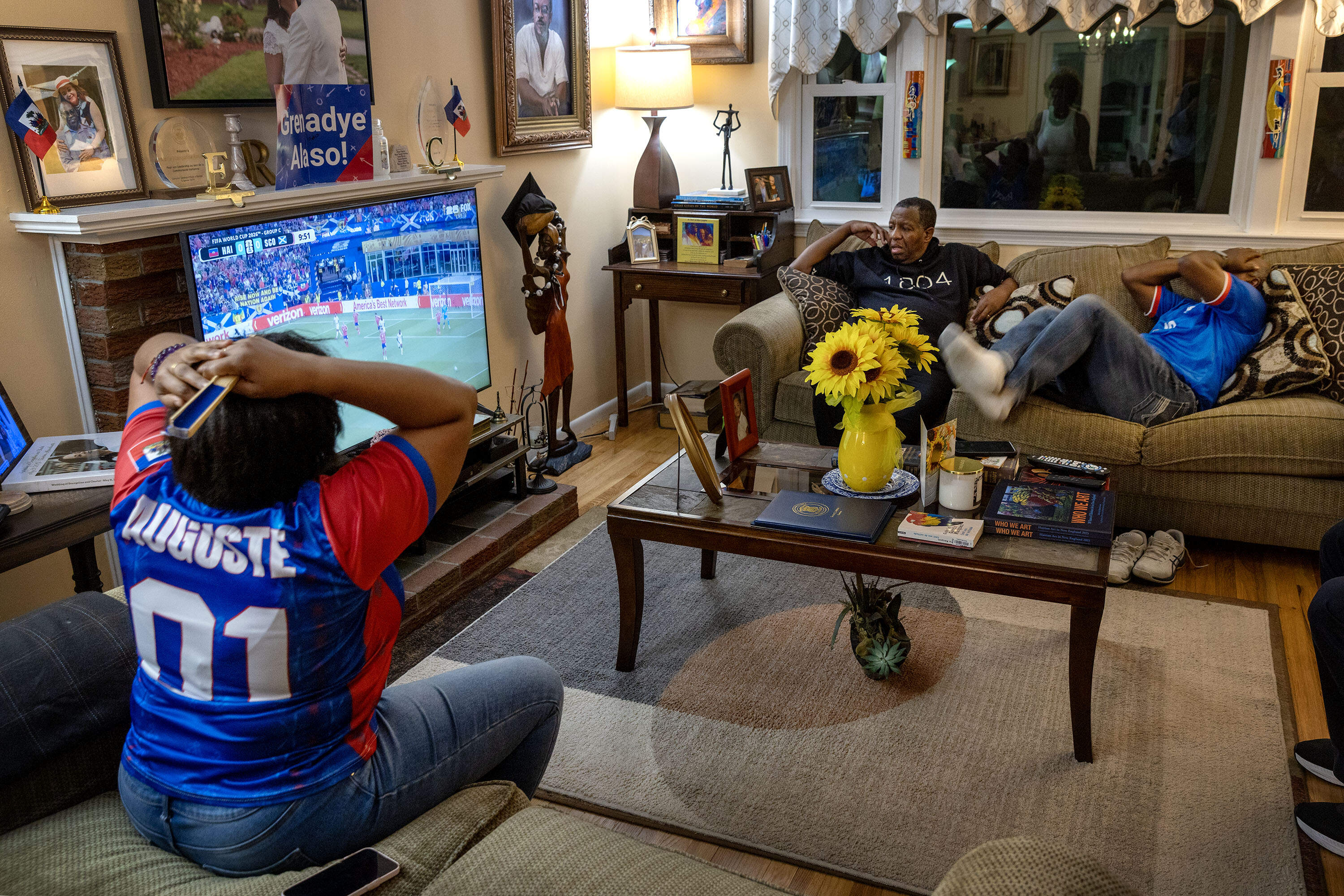 Some of Charlot and Marie Evangeline's watch party guests react as Scotland puts pressure on the Haiti team at the 2026 Men's Soccer World Cup. (Robin Lubbock/WBUR)