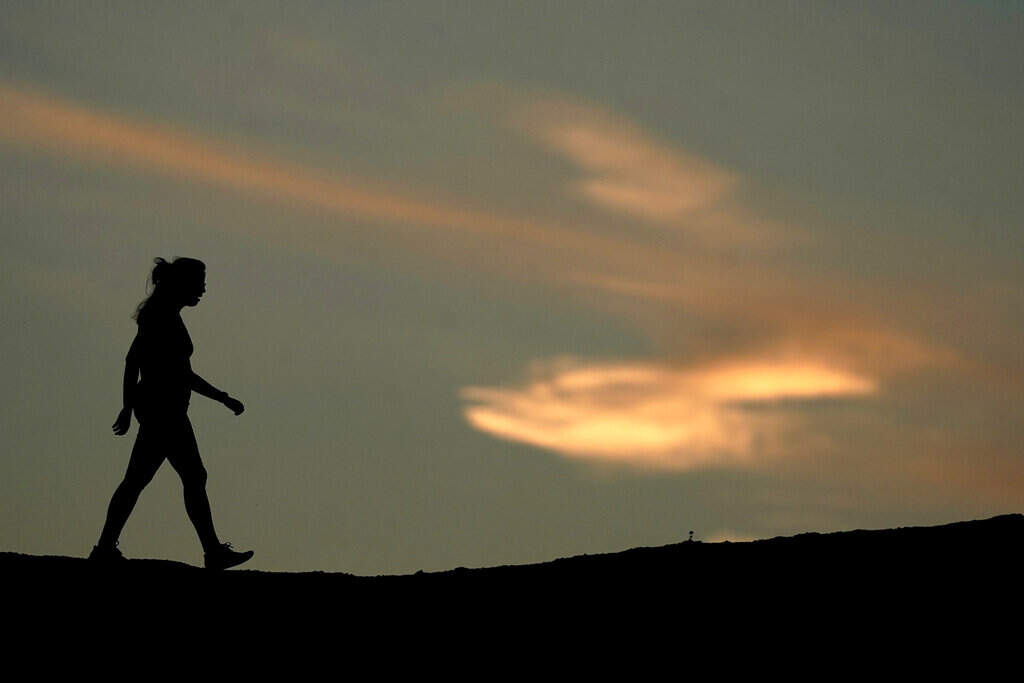 A woman is silhouetted against the sky at sunset as she hikes in Papago Park, Saturday, April 2, 2022, in Phoenix. (AP Photo/Charlie Riedel)
