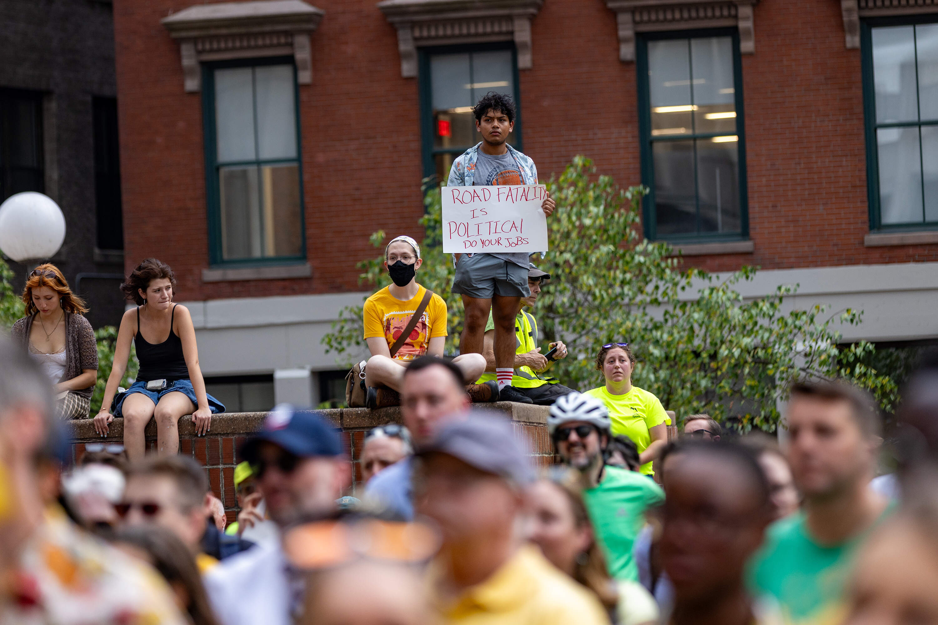 An attendee holds up a sign reading "Road fatality is political, do your jobs" at the vigil for cyclist Louisa Gag. (Jesse Costa/WBUR)