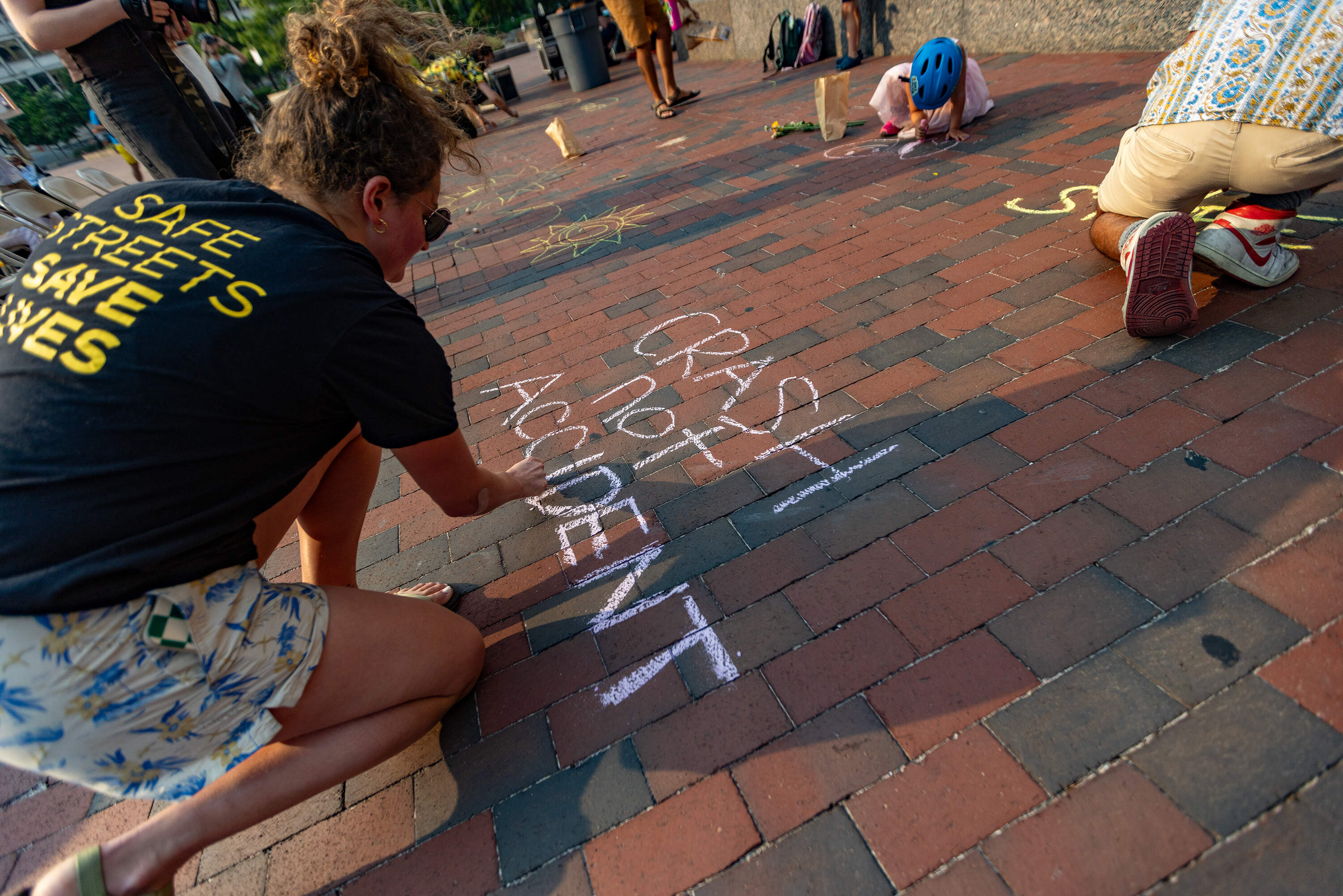 Alexa Gomberg writes the words “Crash not Accident" in chalk on the bricks of City Hall Plaza during a vigil for Louisa Gag. (Jesse Costa/WBUR)