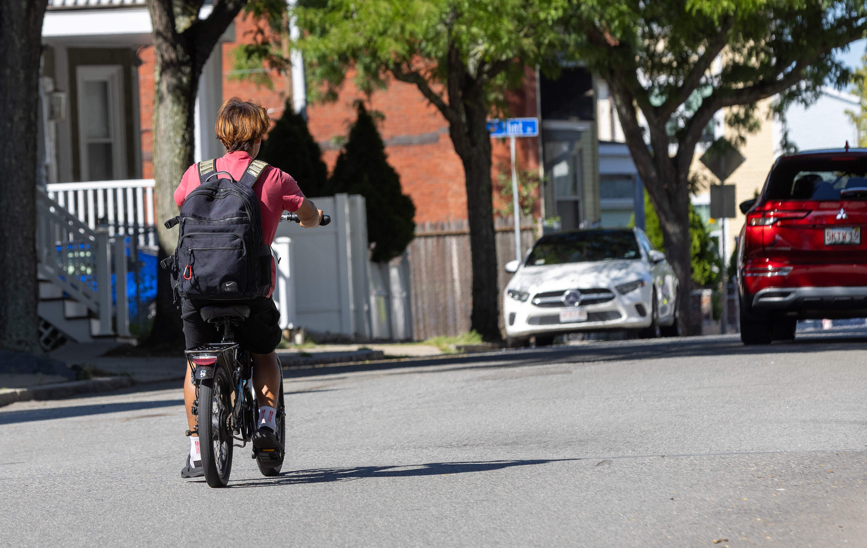 A young teen drags his foot across the road as he rides an e-bike while moving in traffic on Cross Street in Somerville. (Jesse Costa/WBUR)