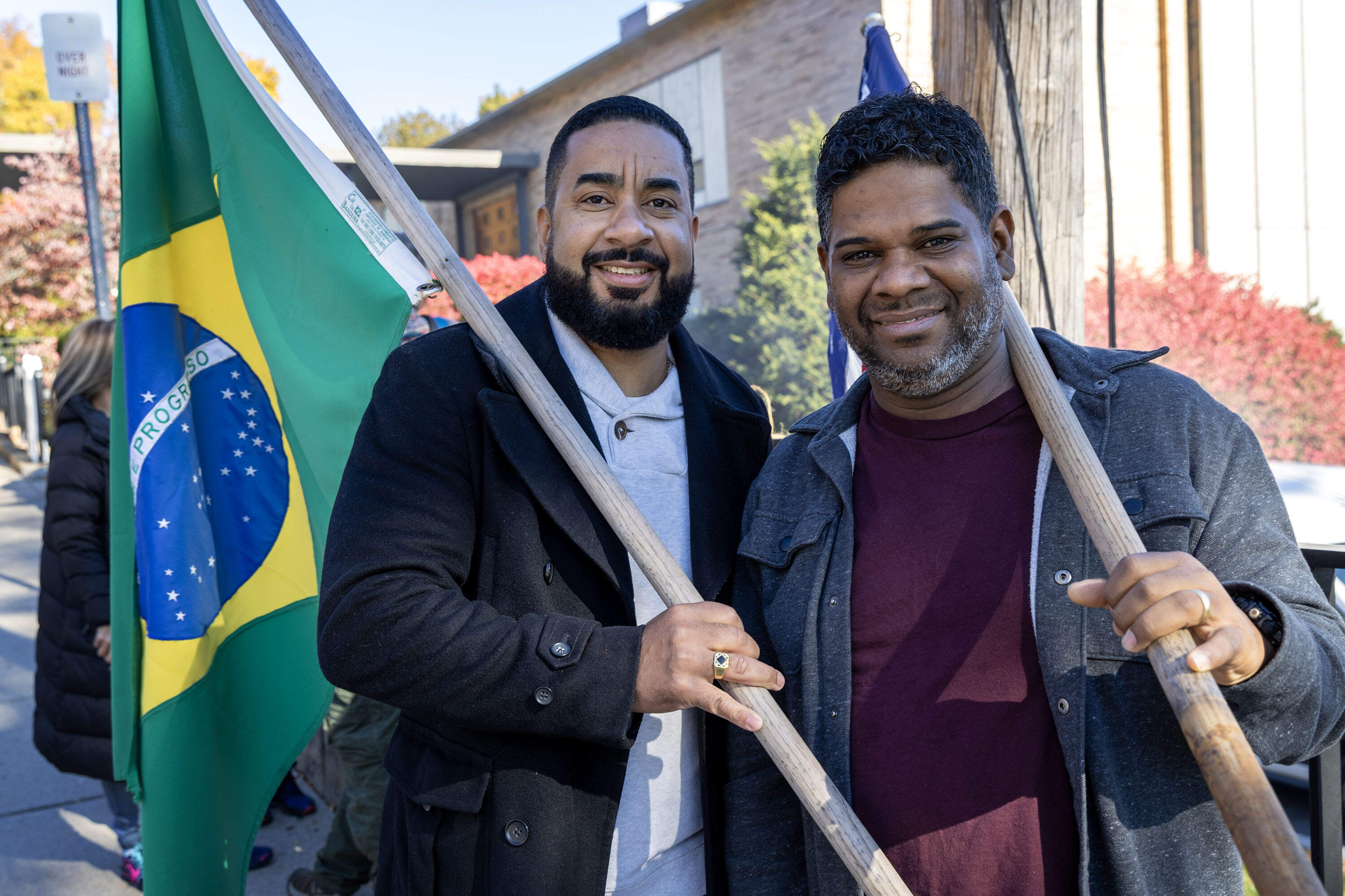 Bolsonaro voters Edson Borges and Nilo Nunes hold flags outside the polling place at Salemwood School in Malden, Mass. (Robin Lubbock/WBUR)
